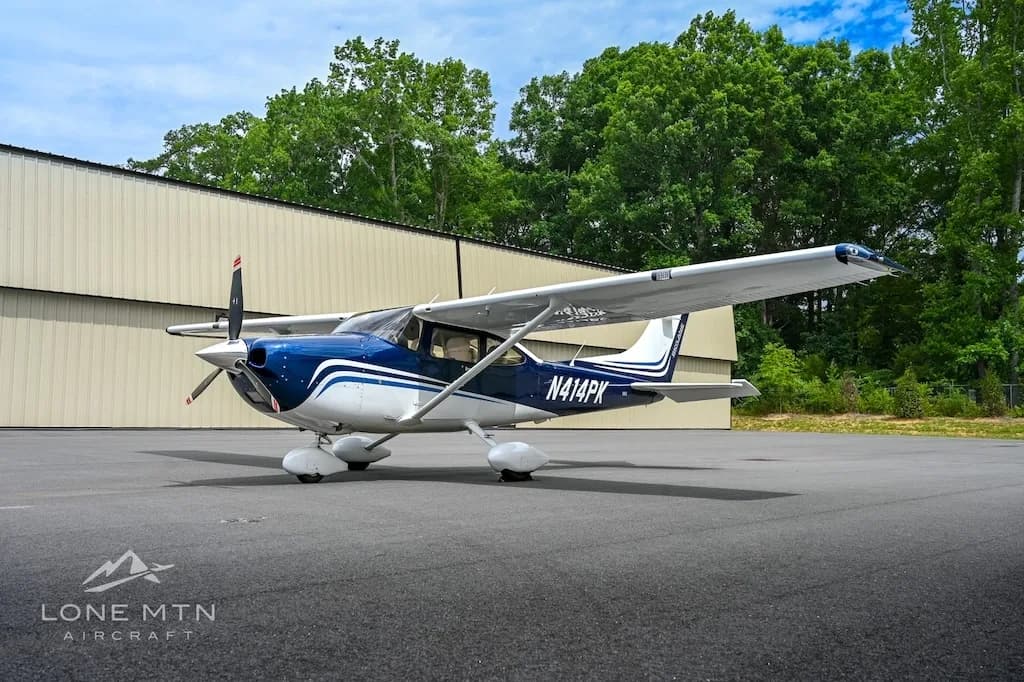 A three-quarter front view of a blue and white Cessna Skylane N414PK parked on an asphalt ramp.