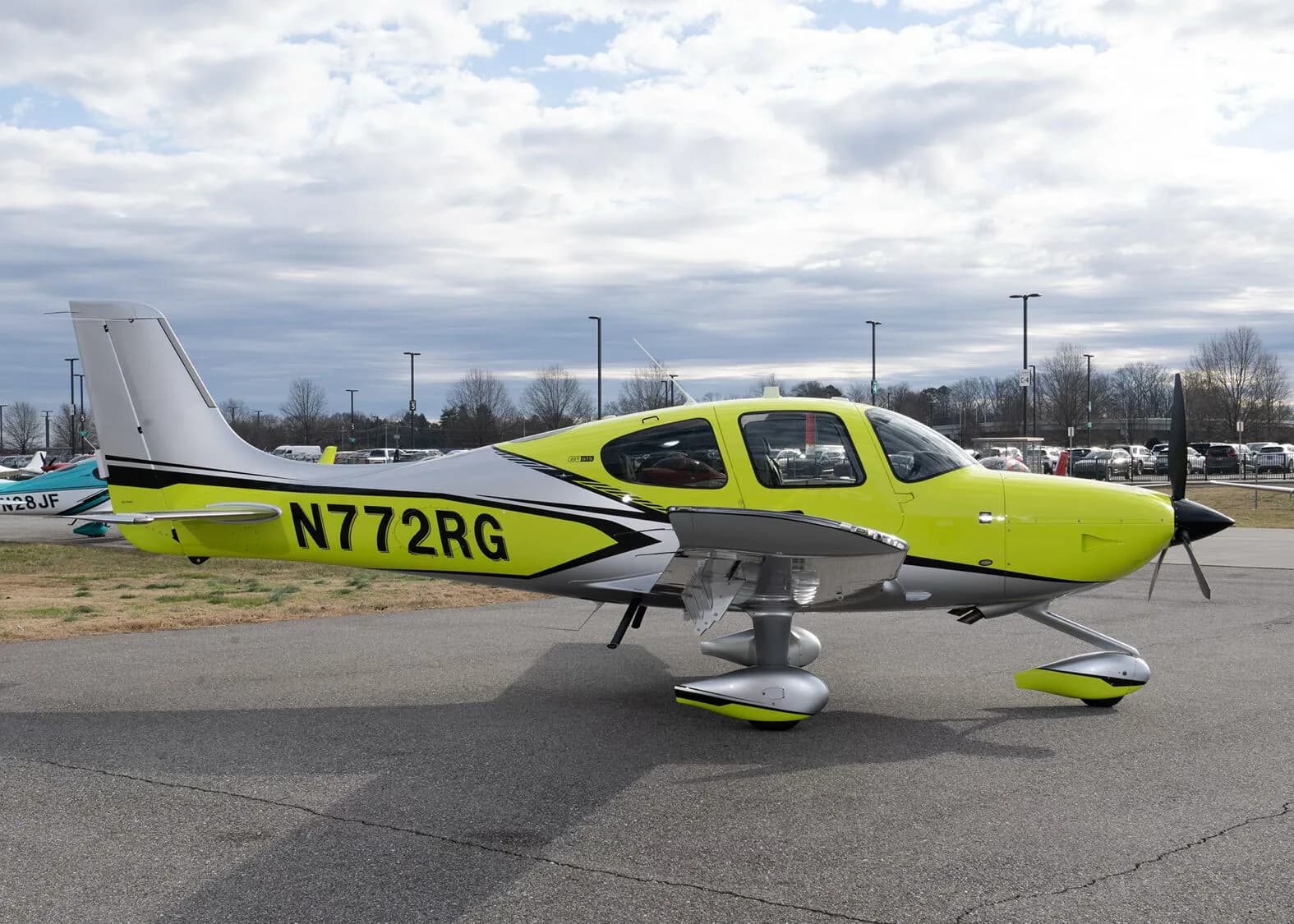 A side view of a yellow and silver Cirrus SR22 aircraft, N772RG, parked on an airport tarmac under a cloudy sky.