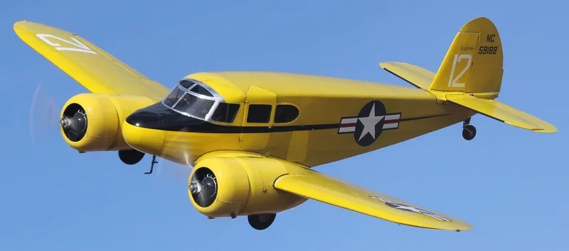 A yellow Beechcraft Model 18 flying in the sky.
