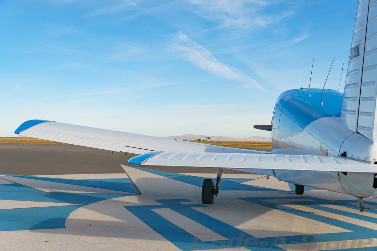 A rear view of the blue and white single-engine aircraft N8718N, highlighting the tail and wing on a patterned tarmac.