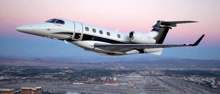 Phenom 300 in flight over a city at sunset.