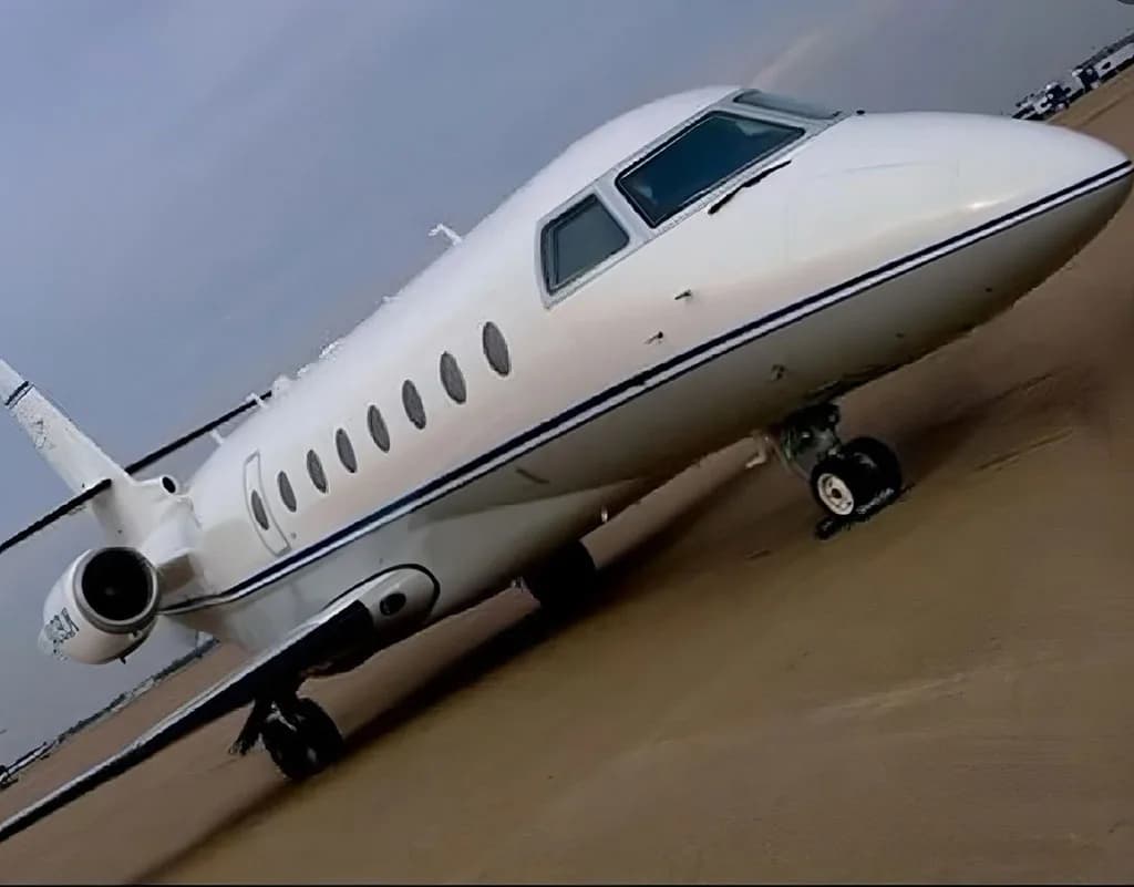 A low-angle view of a white business jet, N409BM, with blue stripes, parked on a tarmac under a cloudy sky.