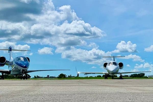Two private jets are parked on an airport tarmac under a partly cloudy sky.