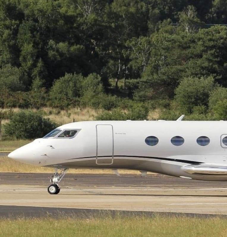 A white aircraft on the runway with green trees in the background.