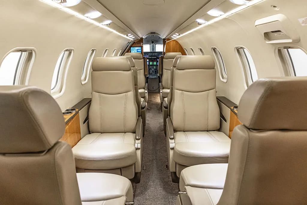 The interior cabin of a private jet with beige leather seats, looking down the aisle towards the cockpit.
