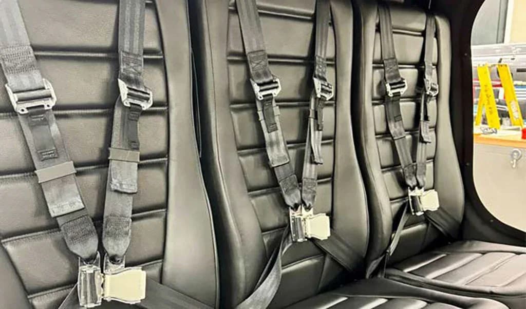 Three black leather passenger seats with safety harnesses are visible inside the helicopter cabin.