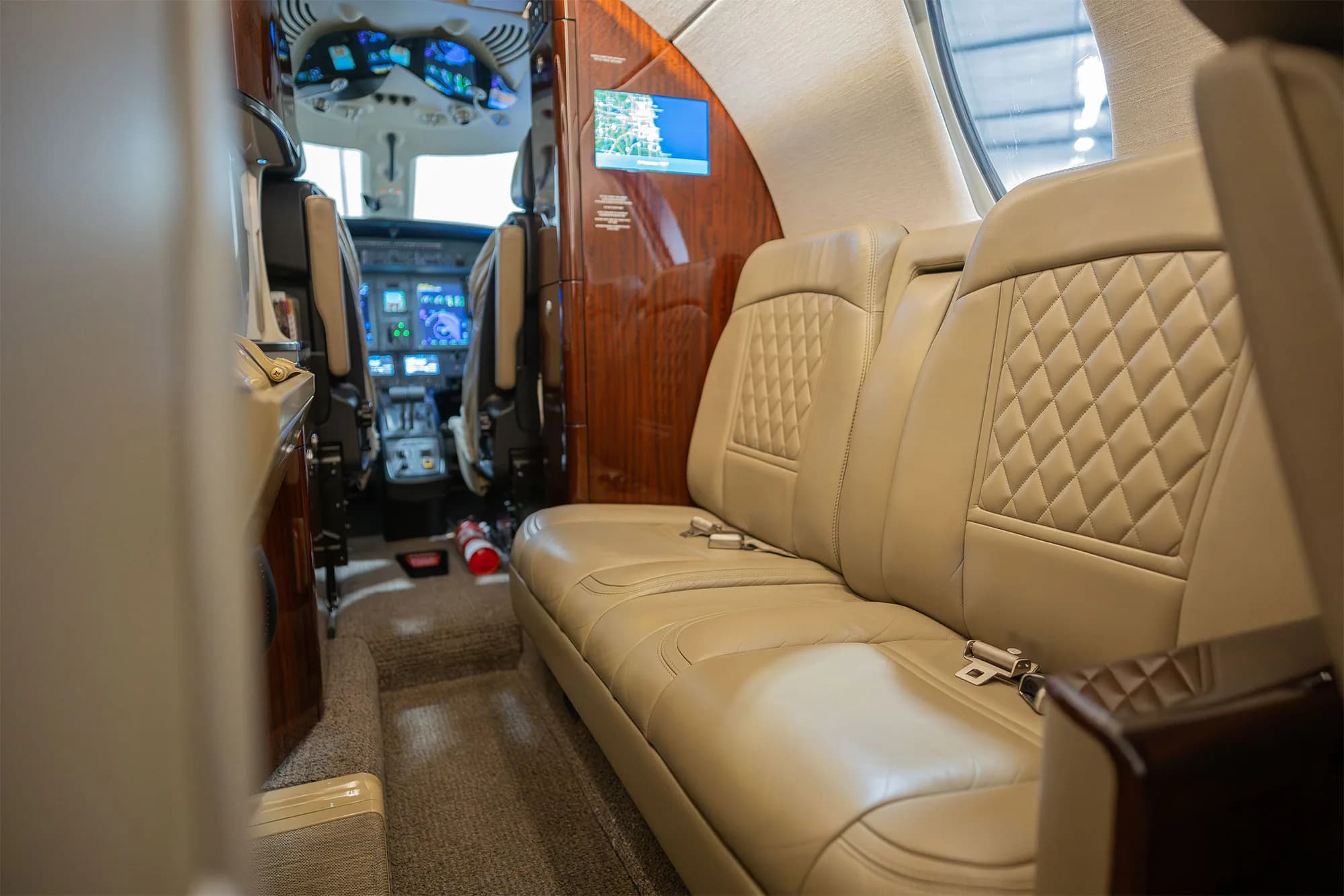 A view from the rear cabin of a business jet, showing beige quilted leather seats and the cockpit in the background.