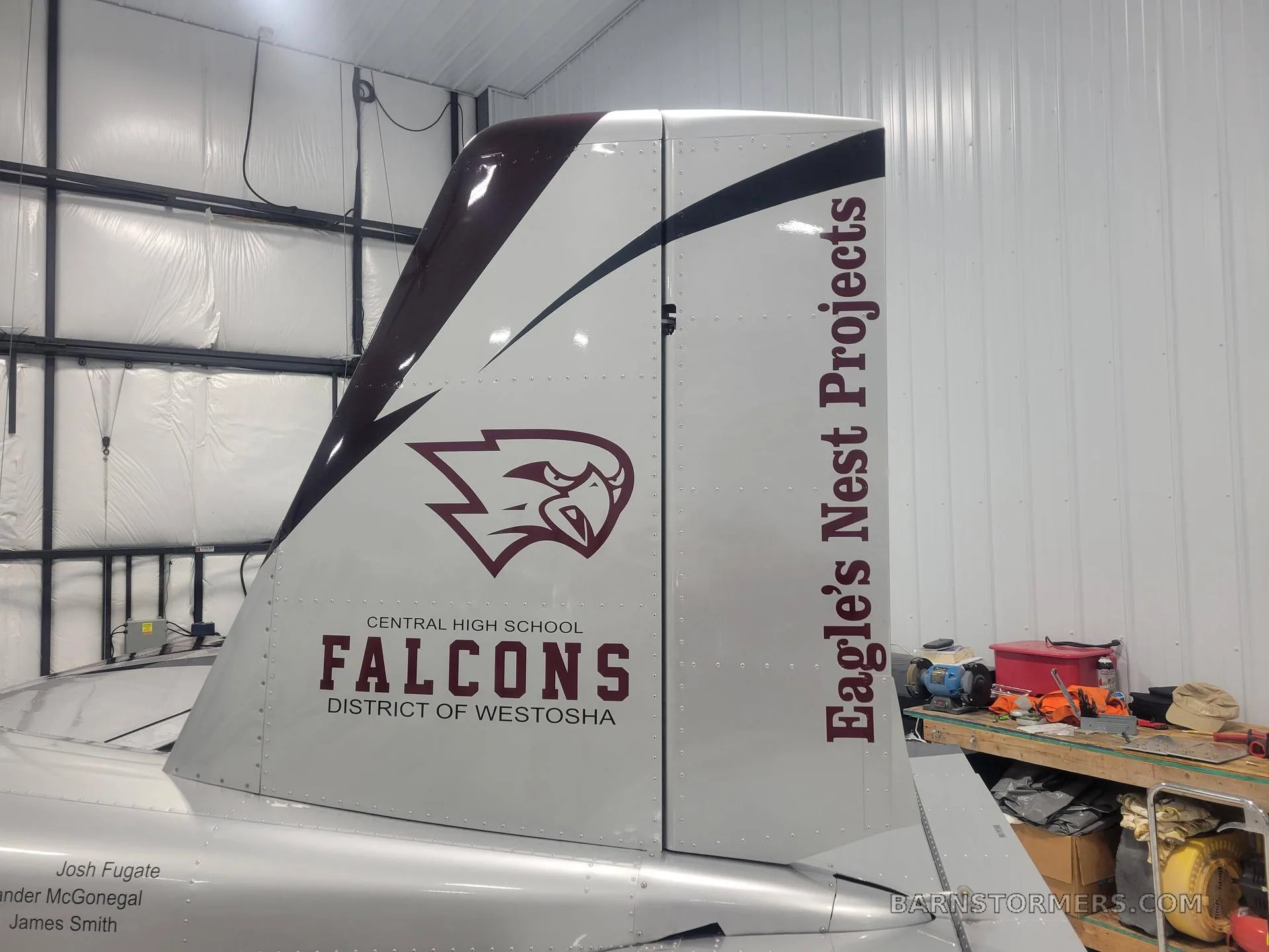 A close-up of the tail of a burgundy and silver aircraft, featuring the 'Falcons' logo and 'Eagle's Nest Projects' text.