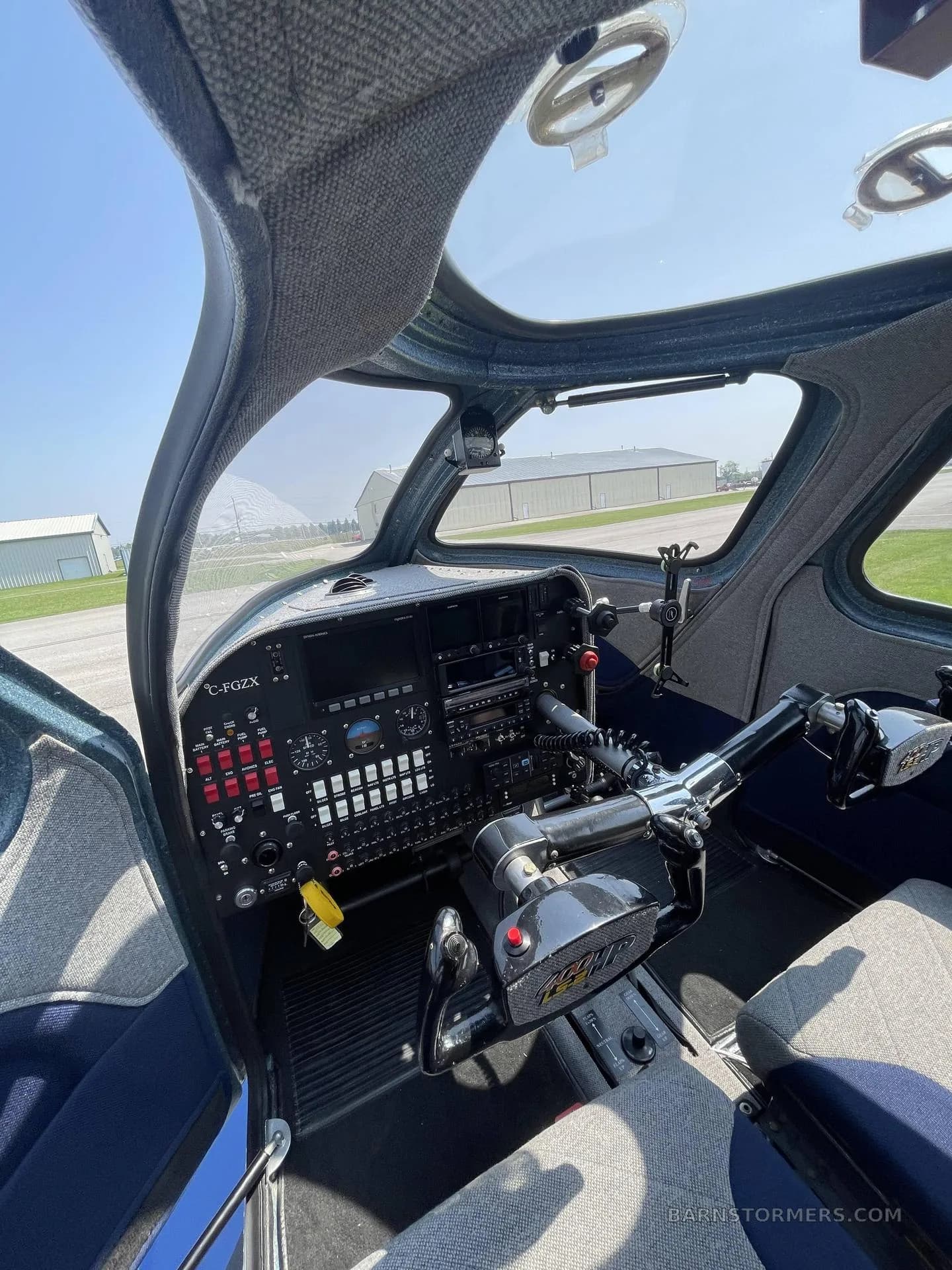 A wide-angle view of an aircraft cockpit interior, showing the instrument panel, control yoke, seats, and the view through the canopy.