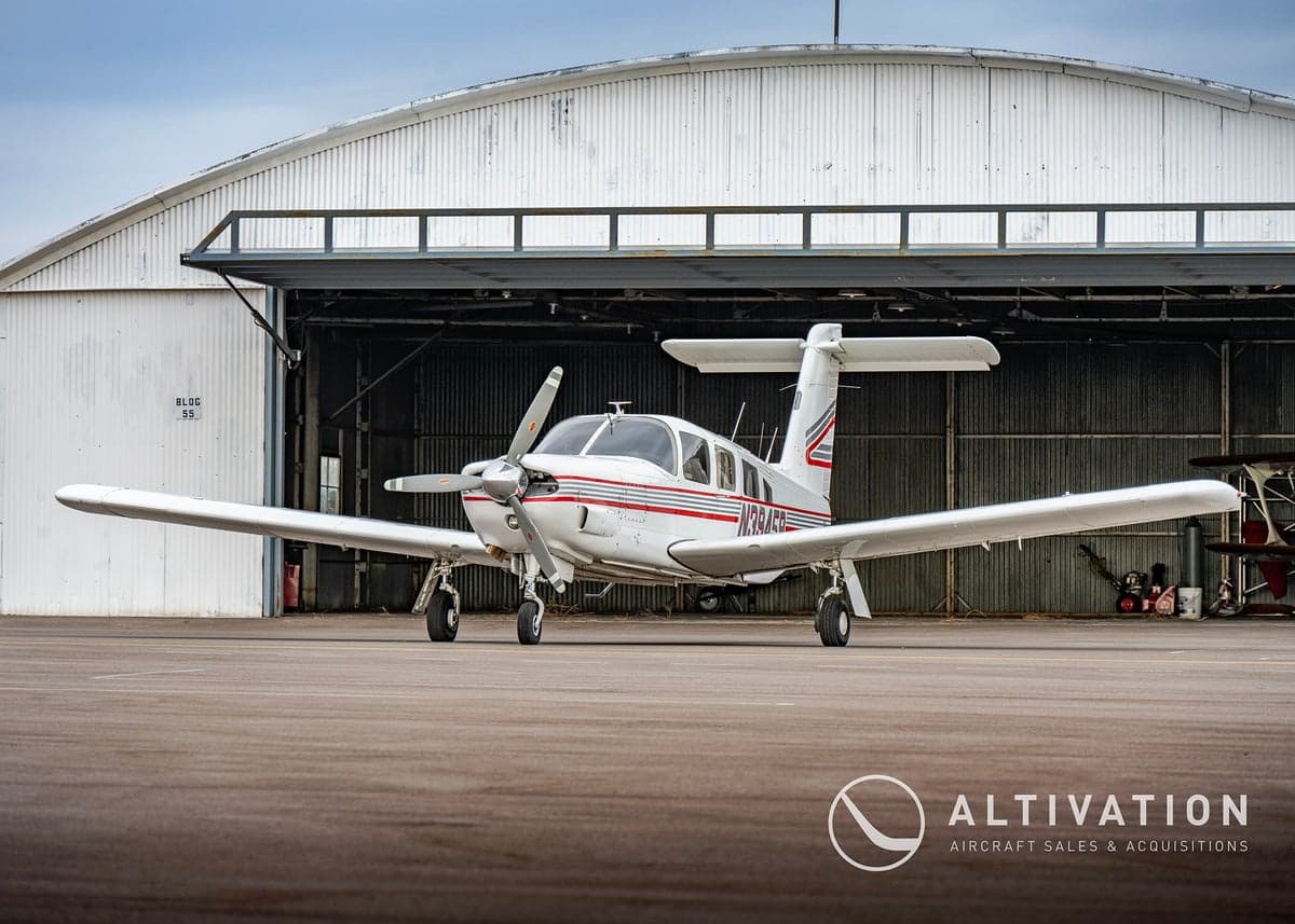 A Piper PA-28-181 Archer II parked in front of an open hangar.