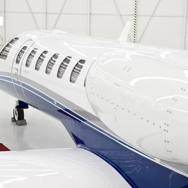 A close-up view of the white and blue fuselage and wing of a private jet inside a hangar.