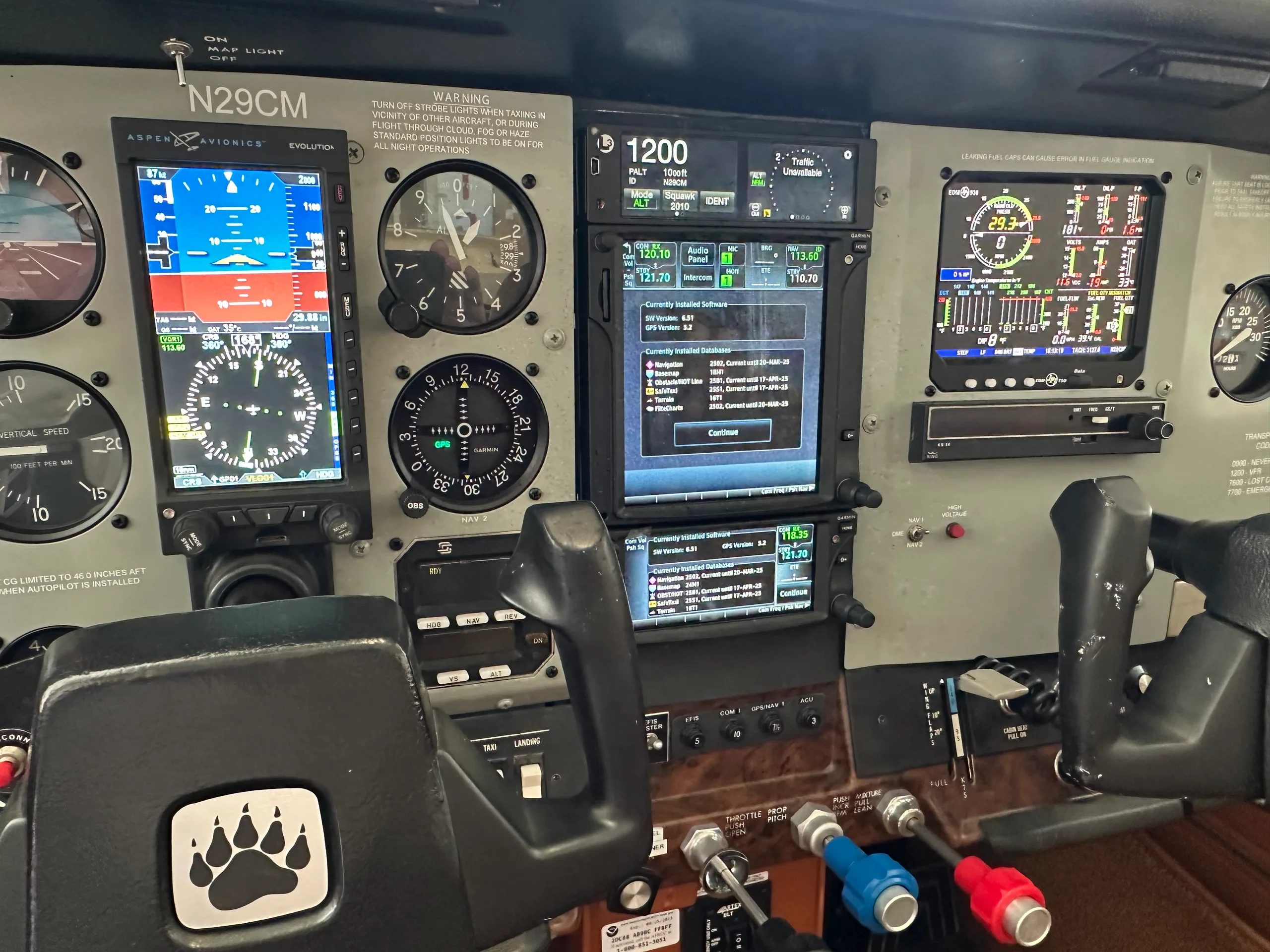 The cockpit instrument panel of an aircraft, featuring both analog gauges and modern digital displays, with a bear paw logo on the yoke.