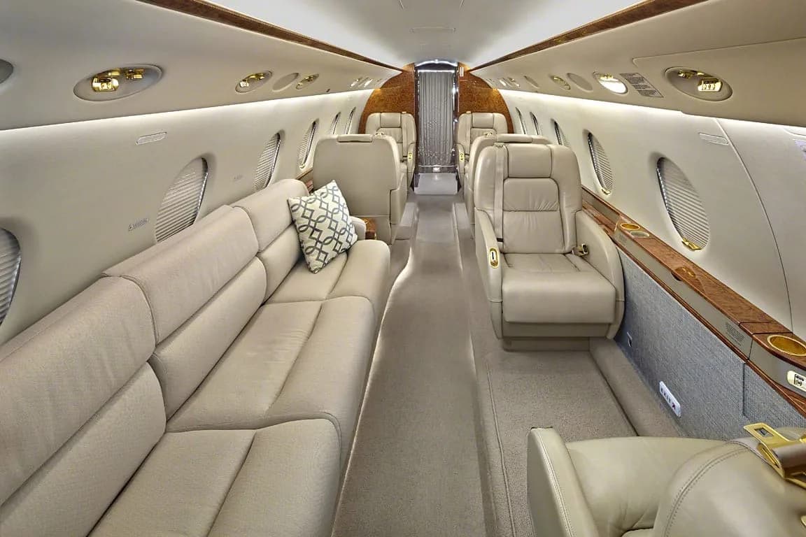The spacious interior cabin of a private jet featuring a long sofa and individual beige leather seats.
