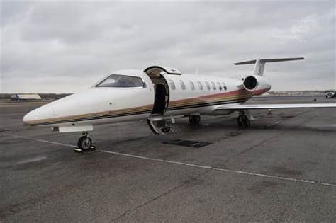 Learjet on the tarmac with an open door and a white and gold paint scheme.