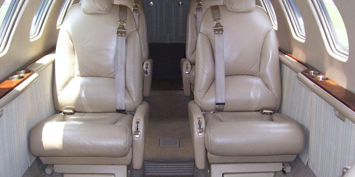 The interior cabin of a private jet, showing two rows of tan leather seats facing each other.