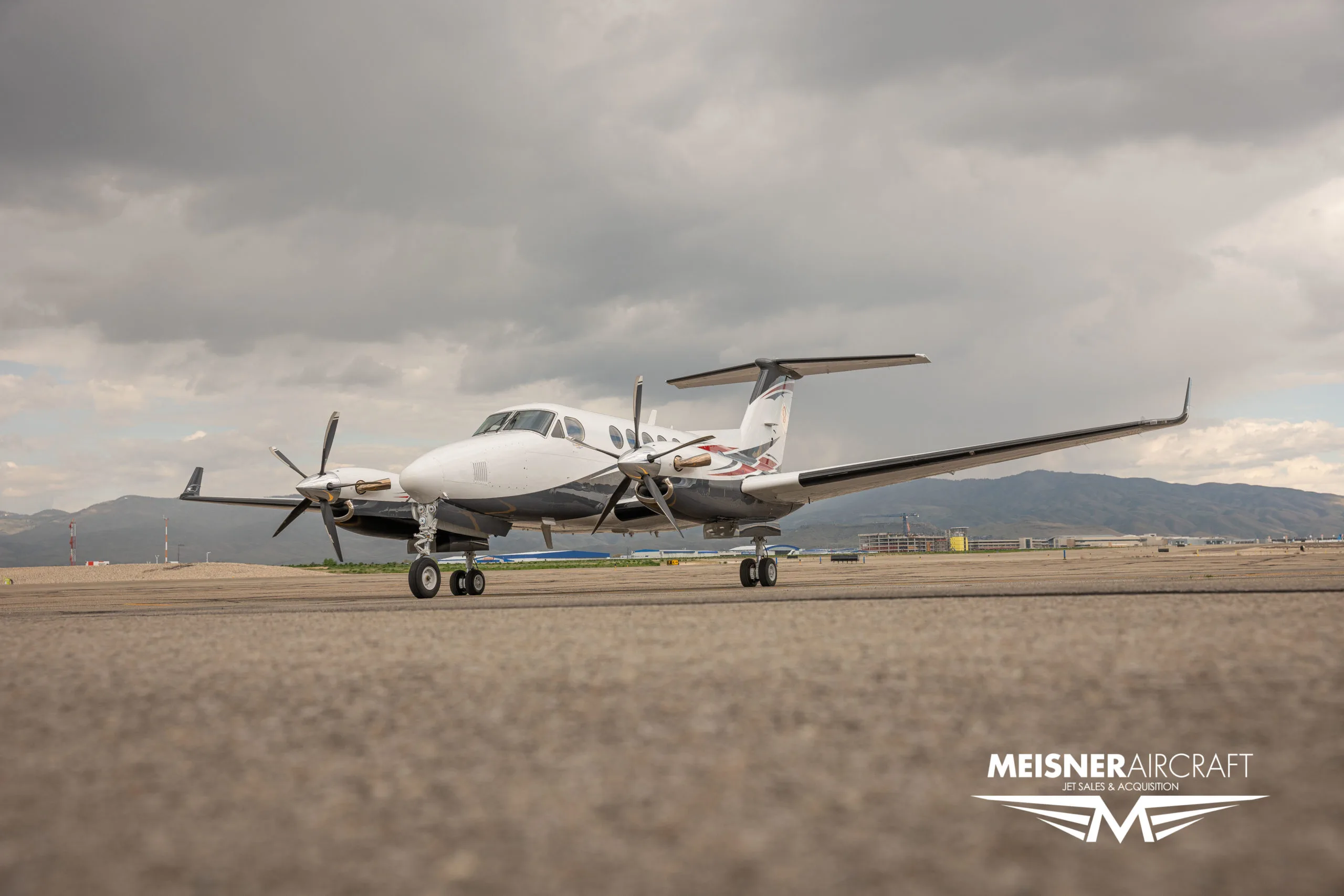 A low-angle view of a white, red, and grey twin-turboprop aircraft on an airport tarmac.