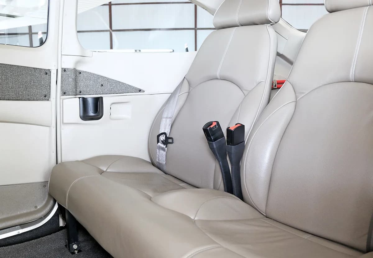 Two light tan leather aircraft seats with seatbelts, viewed from the side.
