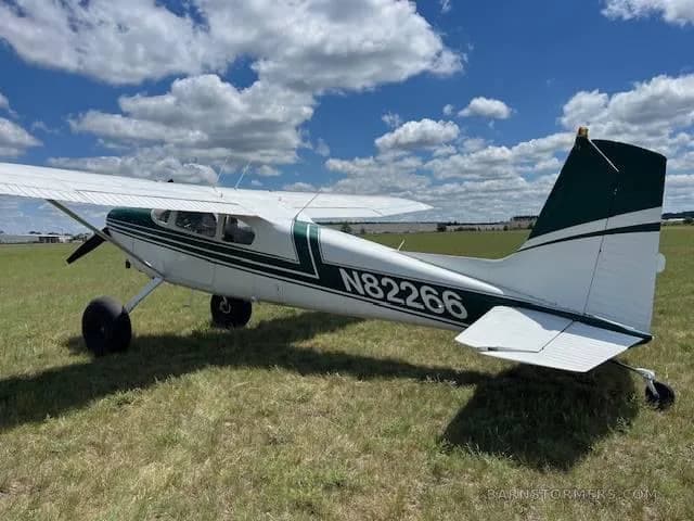 A side view of a white and green single-engine propeller aircraft, registration N82266, parked on a grassy field.