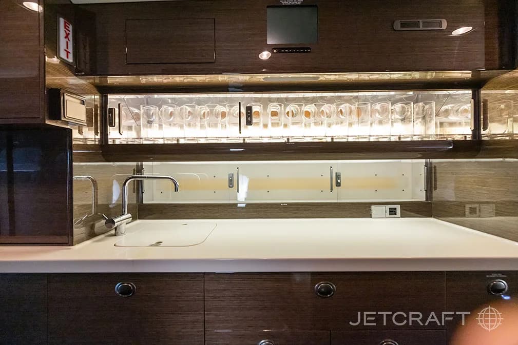 A well-appointed aircraft galley with a sink, countertop, and overhead storage for glassware.