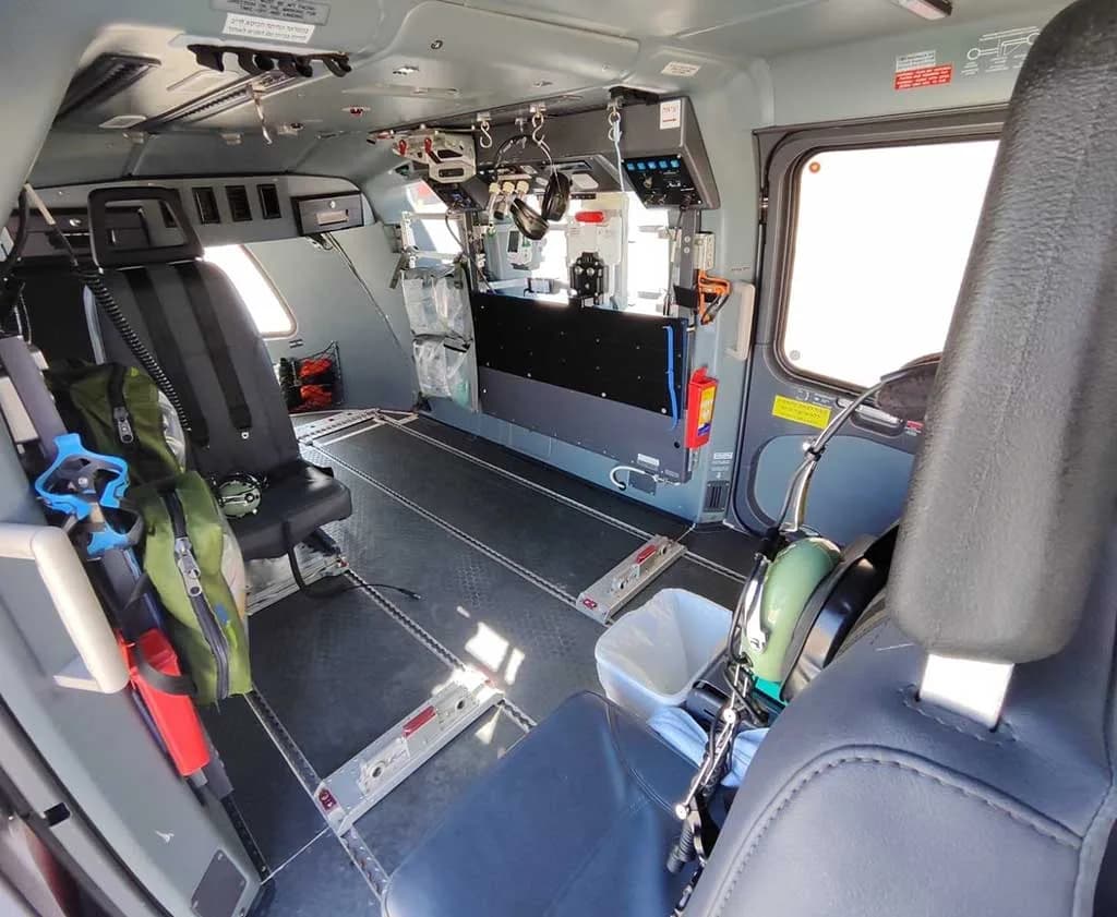 The interior cabin of a helicopter, showing a utility configuration with a single seat and various equipment mounted on the walls.
