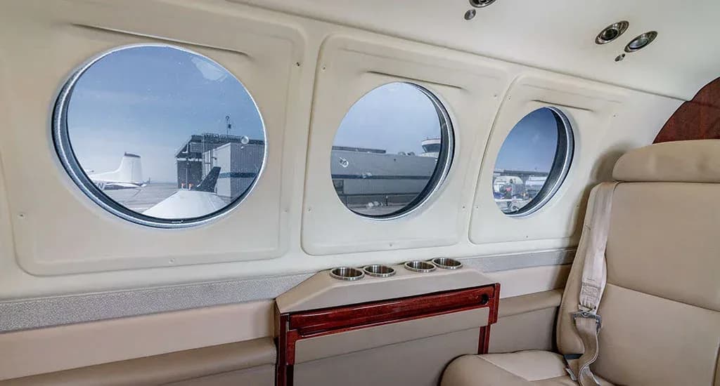 A view from inside an aircraft cabin, showing three round windows looking out onto an airfield.