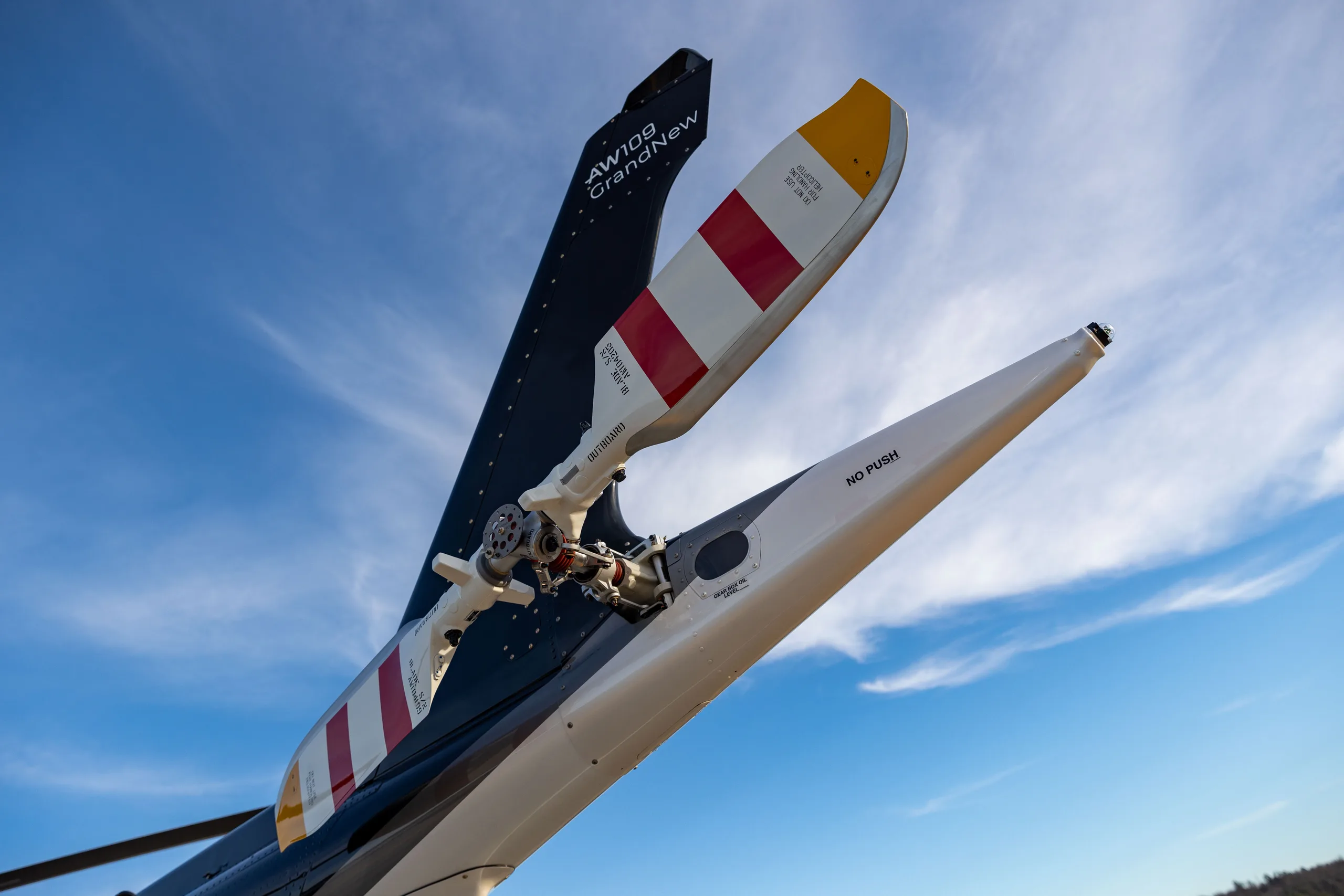 The tail rotor of an AW109 GrandNew helicopter against a blue sky.