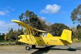 A yellow biplane crop duster sits on the grass under a blue sky.
