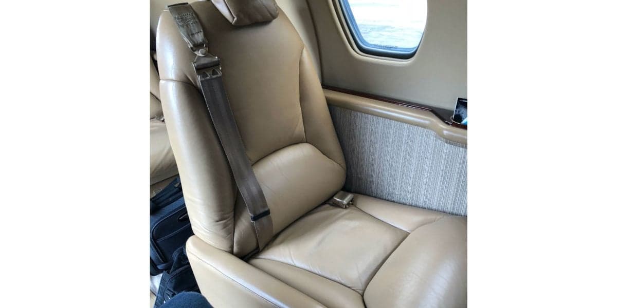 A close-up of a tan leather passenger seat with a seatbelt in the cabin of a private jet.