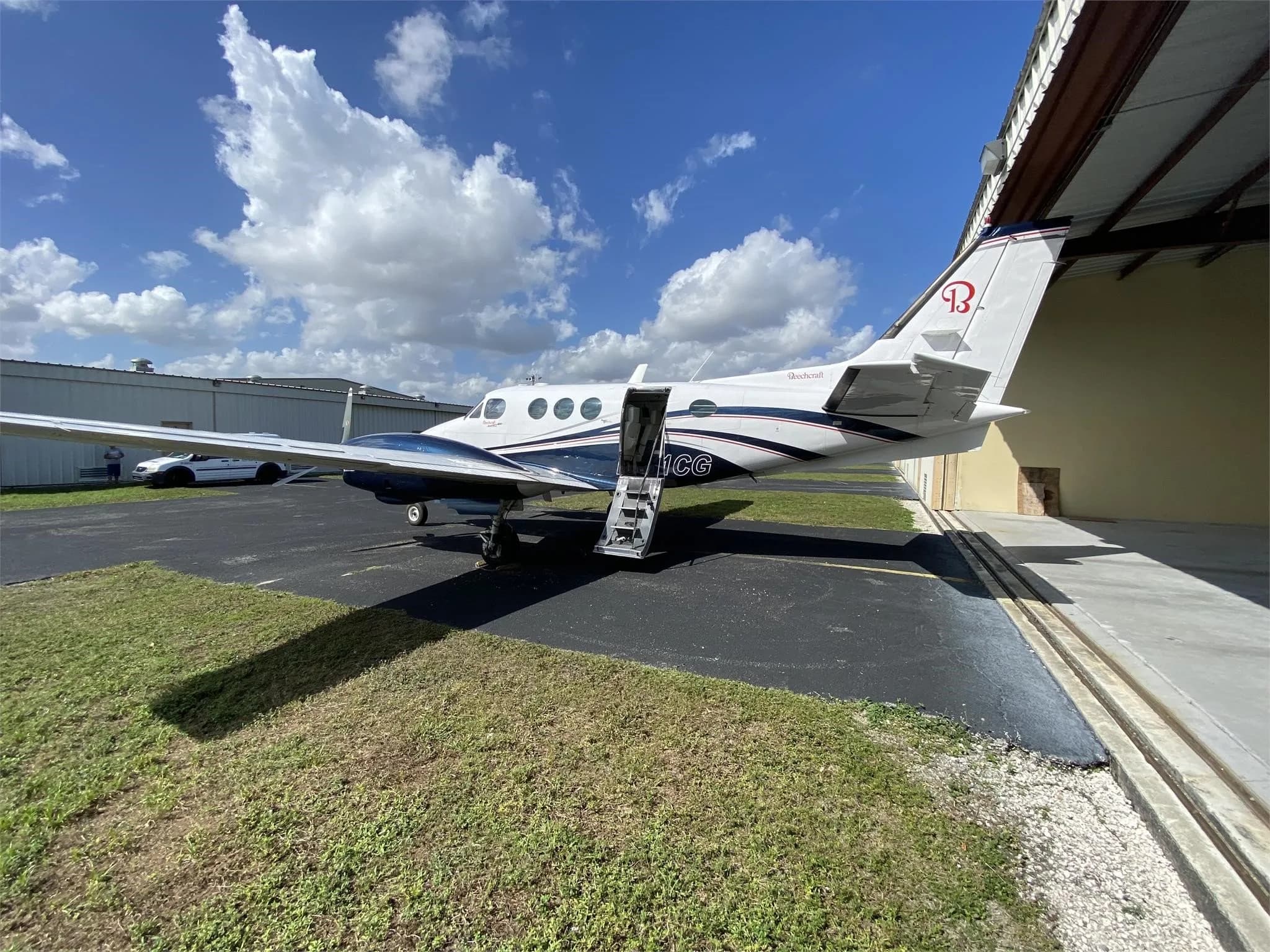 A rear-quarter view of the white and dark blue Beechcraft King Air N211CG with its passenger door open and stairs extended.