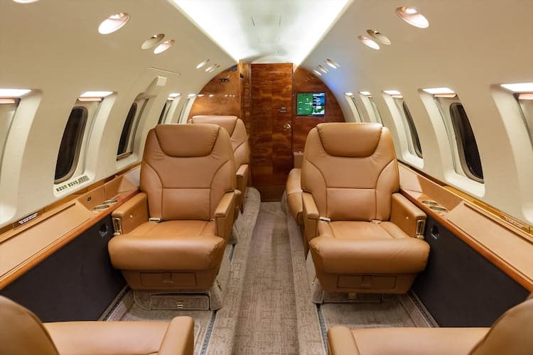 Interior view of a private jet with leather seats and wood trim.