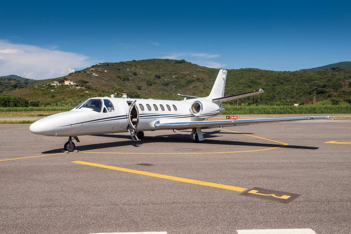 A white jet with an open door sits on the tarmac.