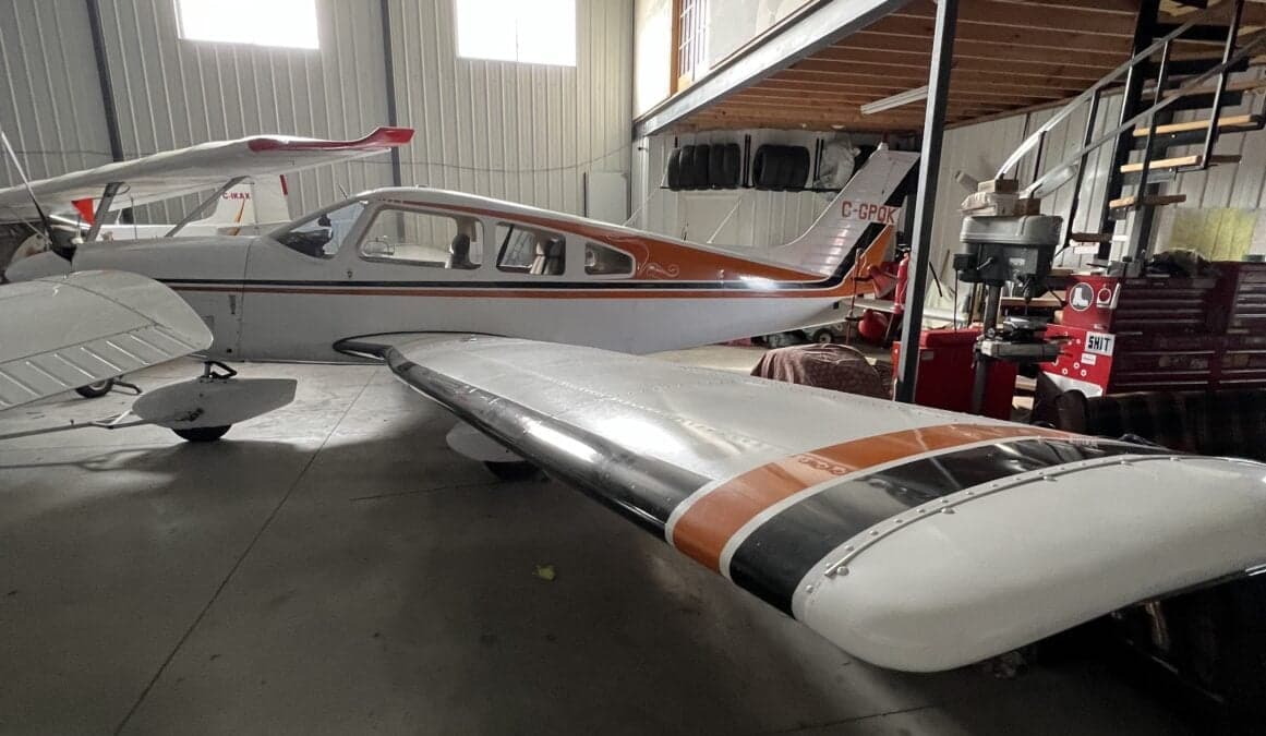 Side view of a white and orange aircraft with tail number C-GPOK, parked in a hangar.