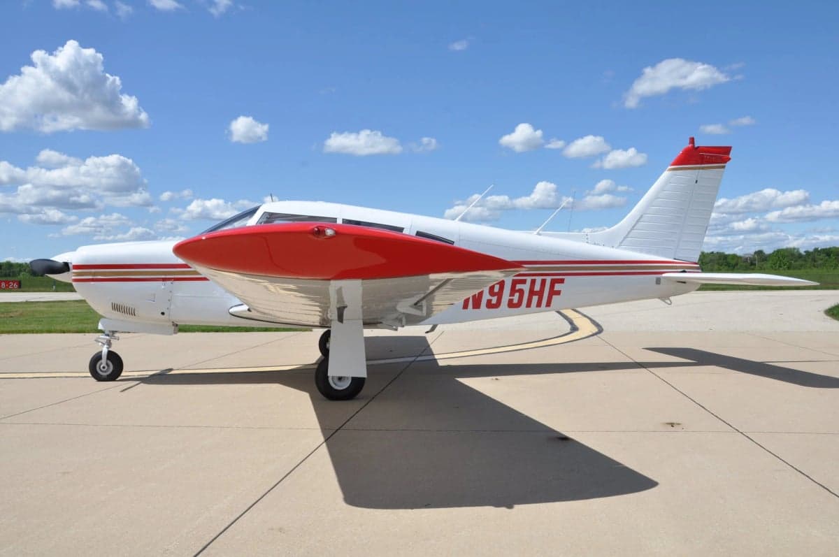A side view of a white single-engine aircraft with red and gold stripes, red landing gear fairings, and registration N95HF.