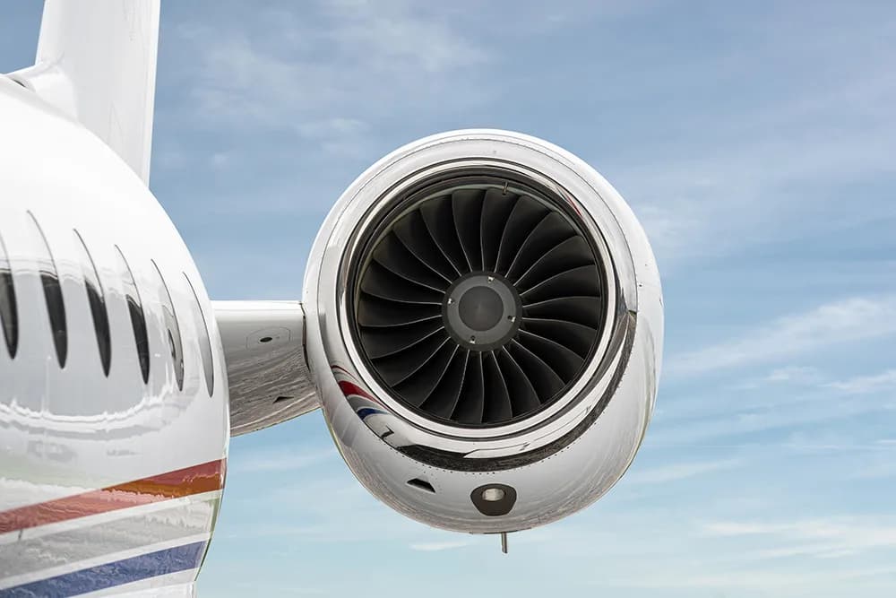 A close-up view of the polished engine intake of a white business jet against a blue sky.