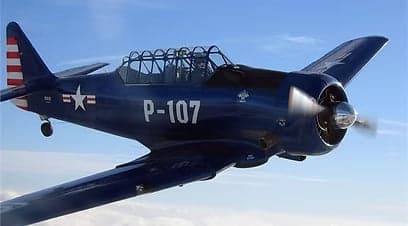 A blue North American Aviation T-6 Texan aircraft in flight with a white star and red and white stripes on the tail.