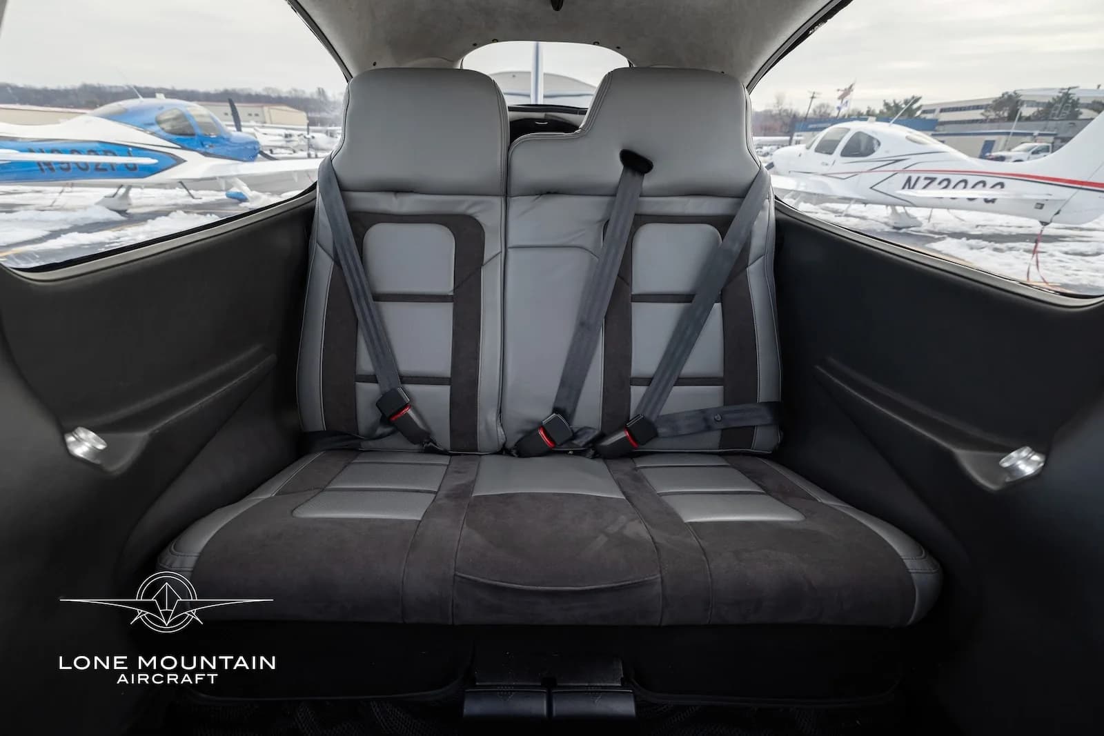 The gray leather and fabric rear seats of the Cirrus SR20 cabin, with other aircraft visible outside.