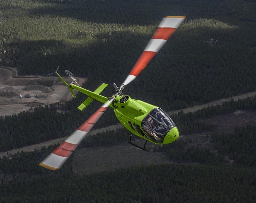 A green helicopter flying over a forest.