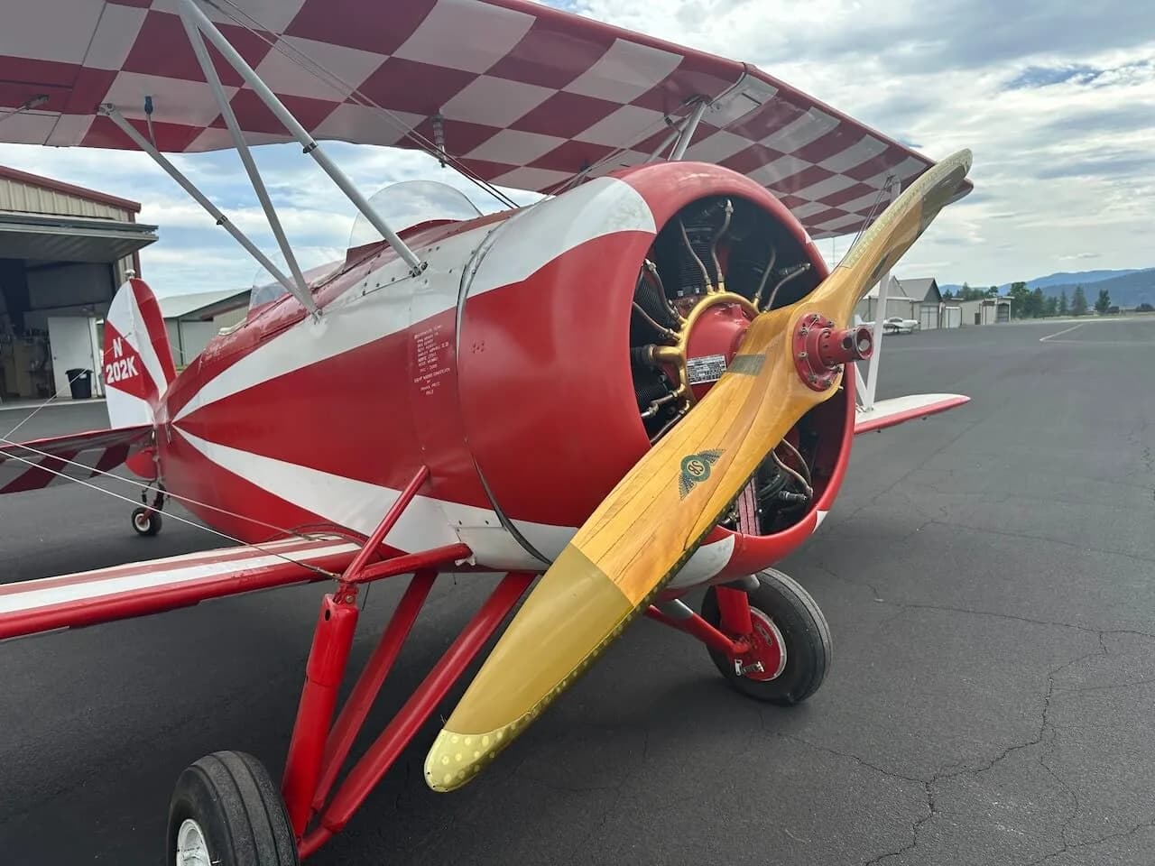 A side view of the red and white biplane, showing its radial engine, wooden propeller, and N202K on the tail.