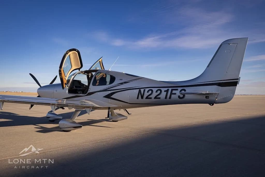 A side view of the silver Cirrus SR22T aircraft N221FS with its doors open, parked on an airfield.
