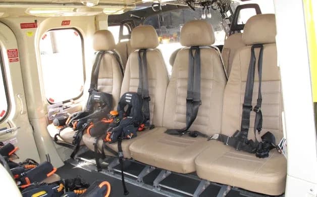 Interior view of a helicopter cabin showing four beige seats with harnesses.