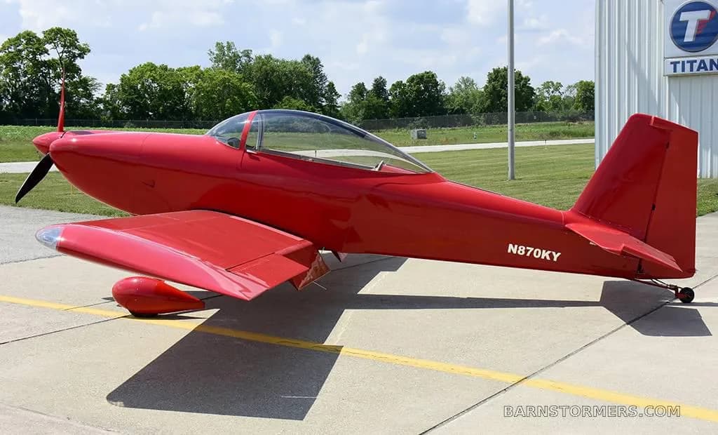A bright red single-engine aircraft, registration N870KY, parked on an asphalt tarmac next to a hangar.