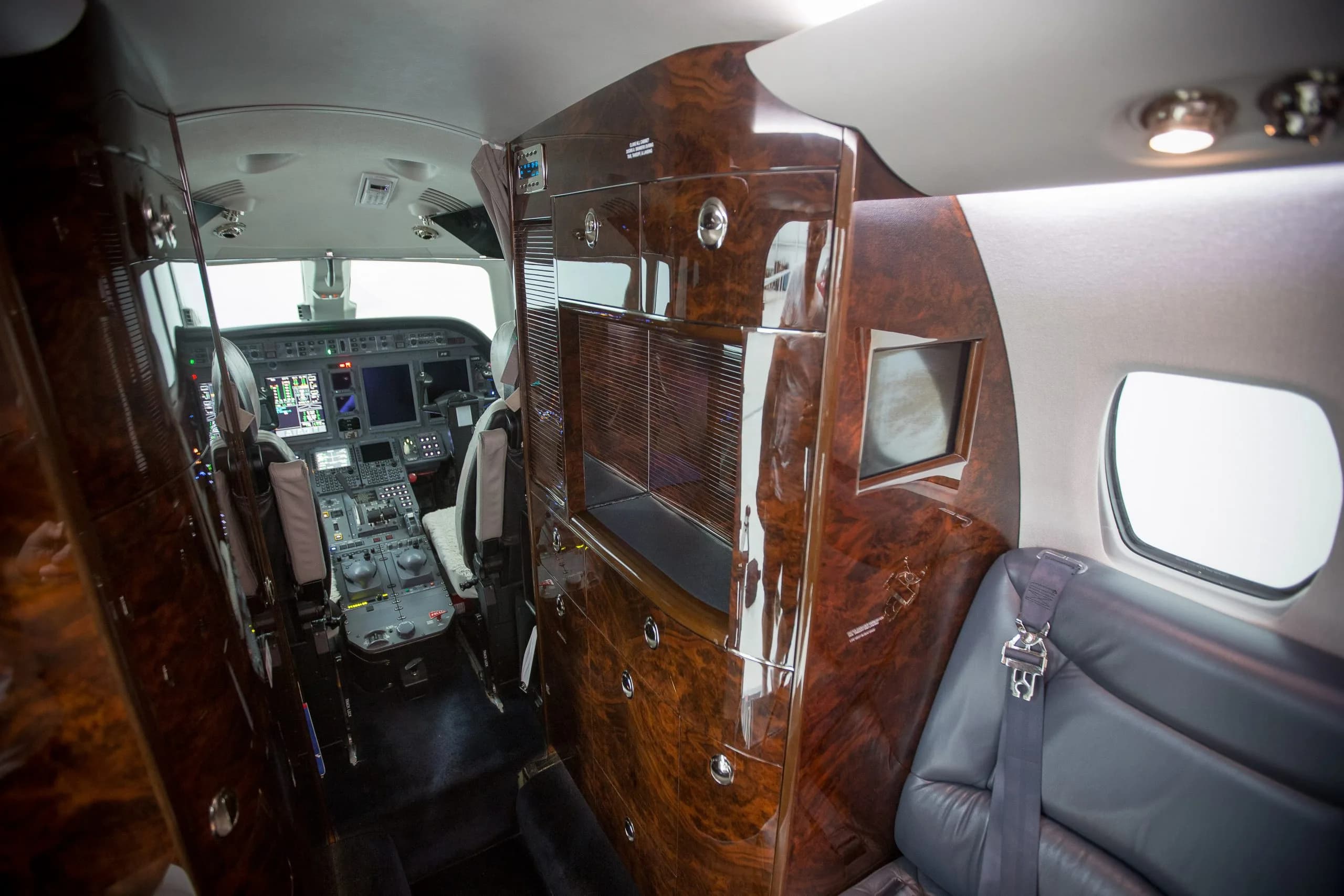 A view of the aircraft cabin with wood trim and a partial view of the cockpit.