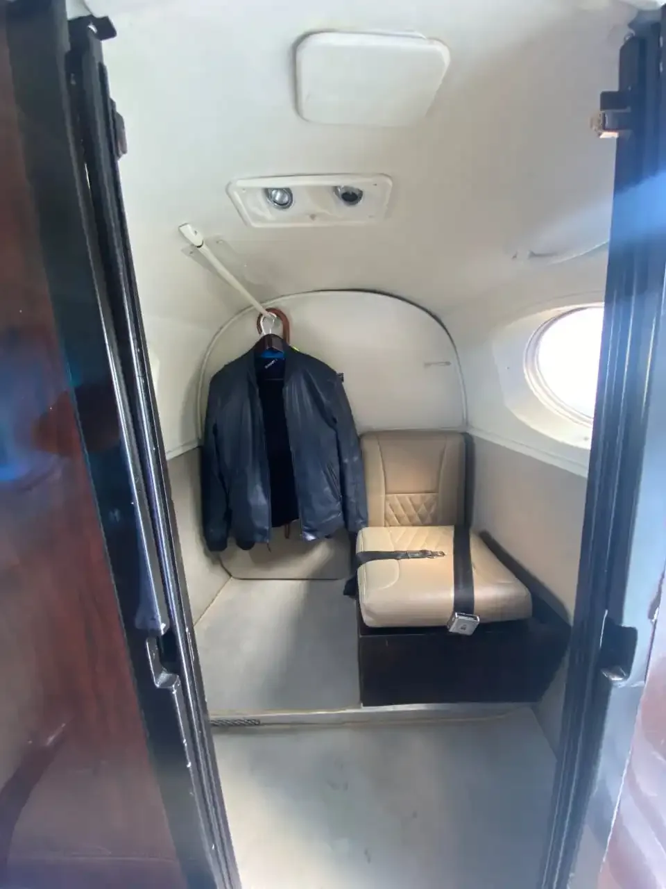 A small section of the aircraft interior with a single tan seat and a jacket hanging.