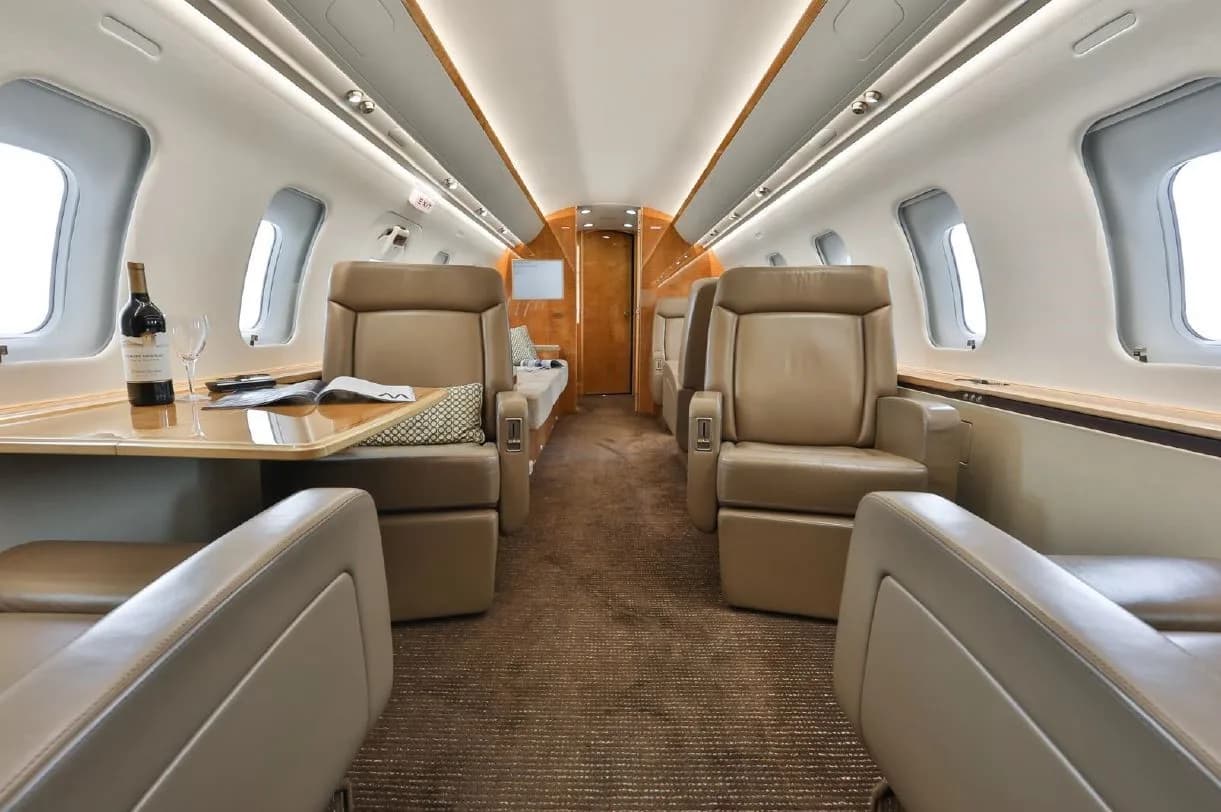A view of the private jet's interior cabin with beige seats, a table set with wine, and elegant wood finishes.