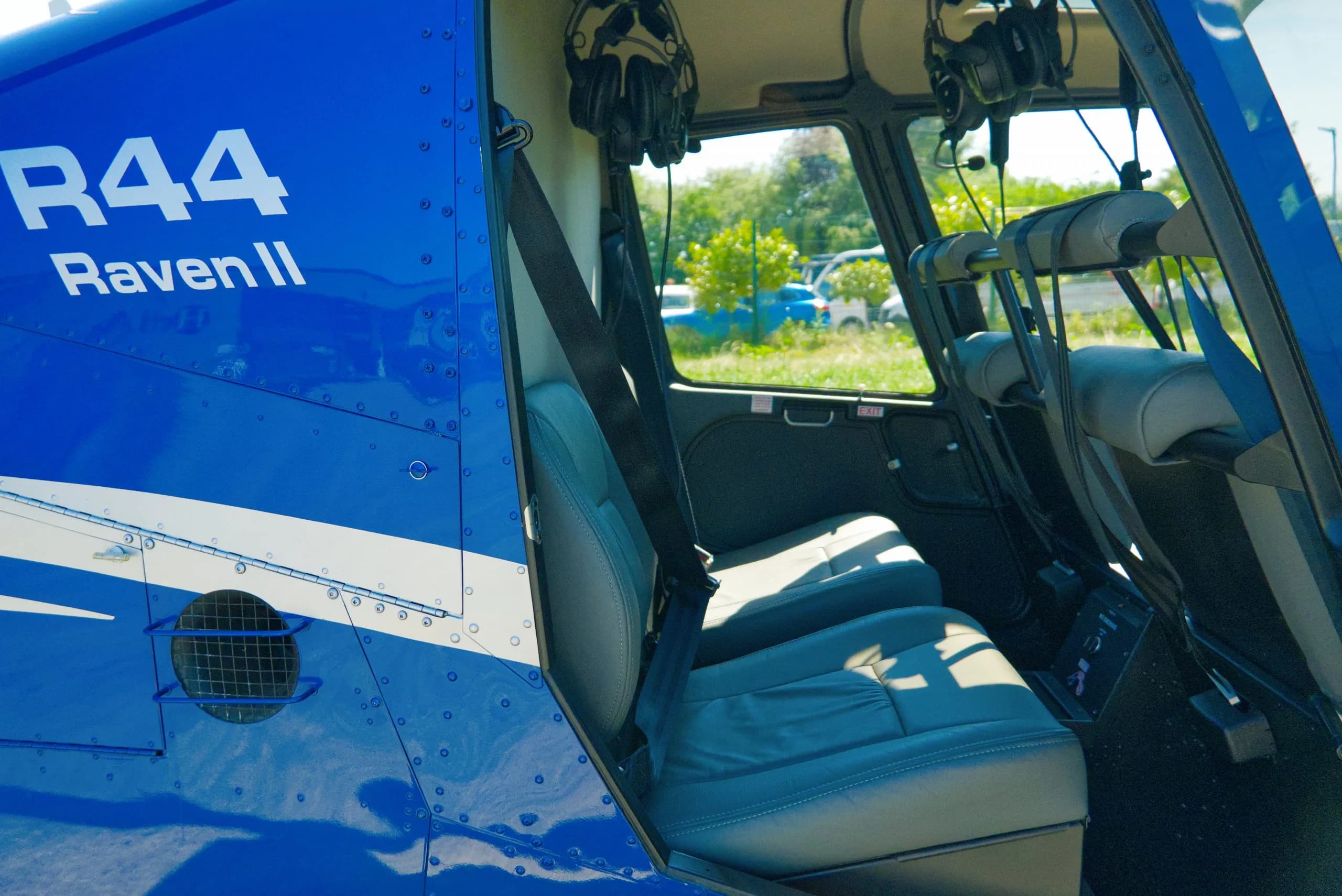 The gray interior cabin seats of a blue Robinson R44 Raven II helicopter are visible.