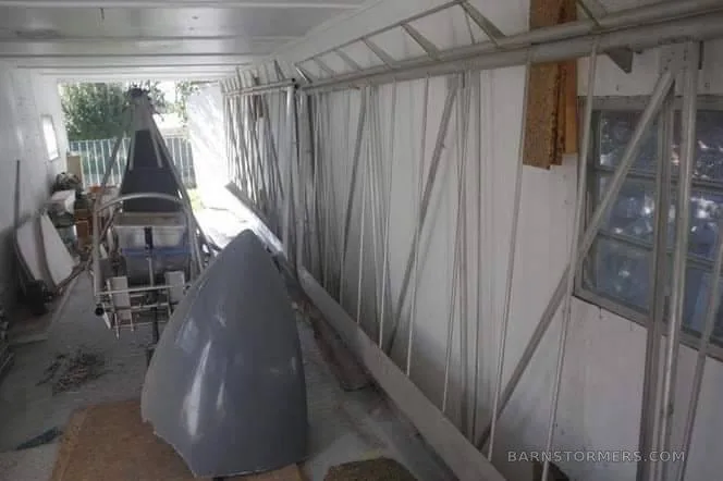 A grey aircraft nose cone or fairing in the foreground, with other aircraft components and a frame in a workshop.