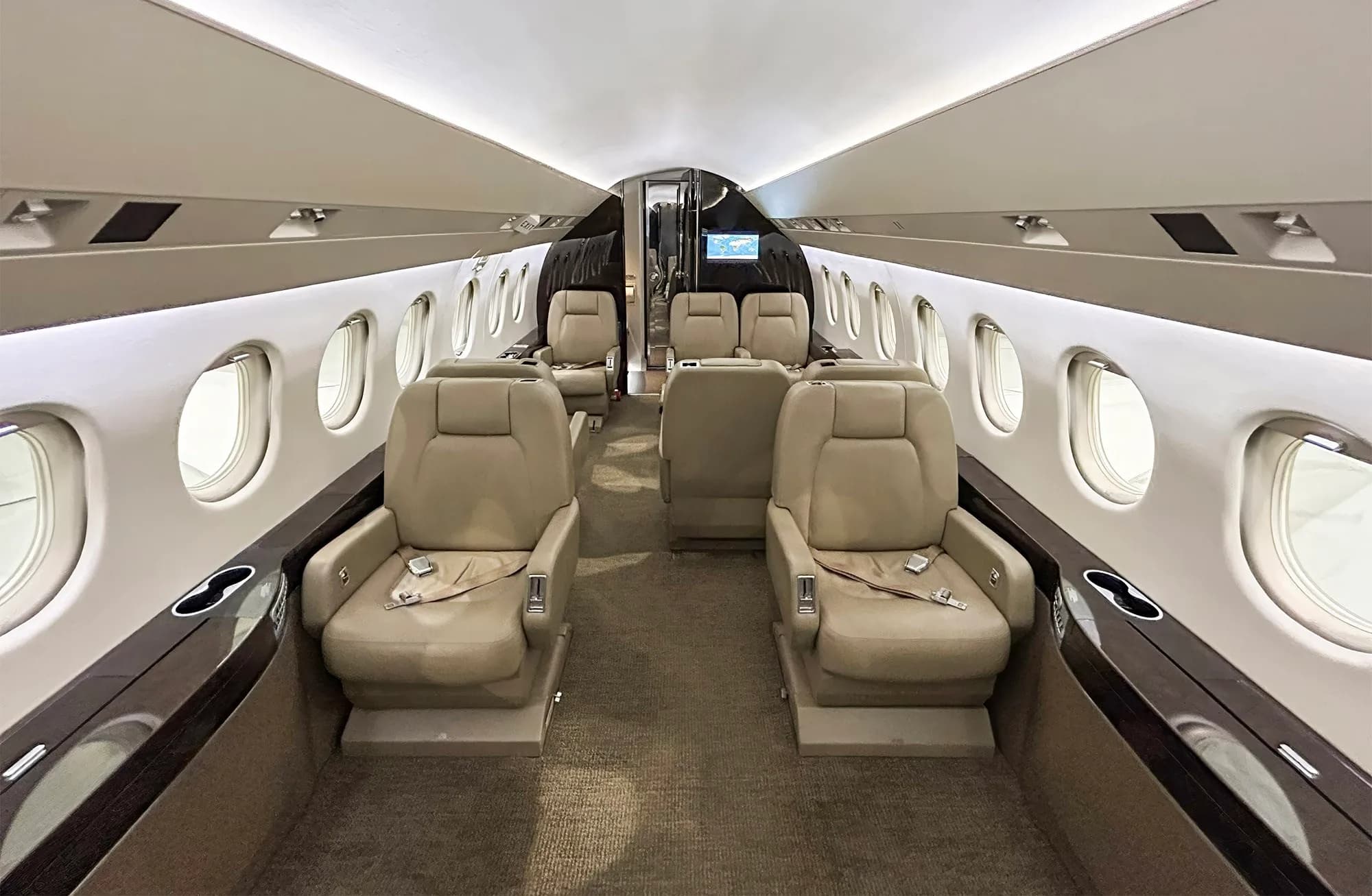 The luxurious cabin interior of a Dassault Falcon 900EX, featuring tan leather seats, dark wood accents, and ample natural light from the windows.