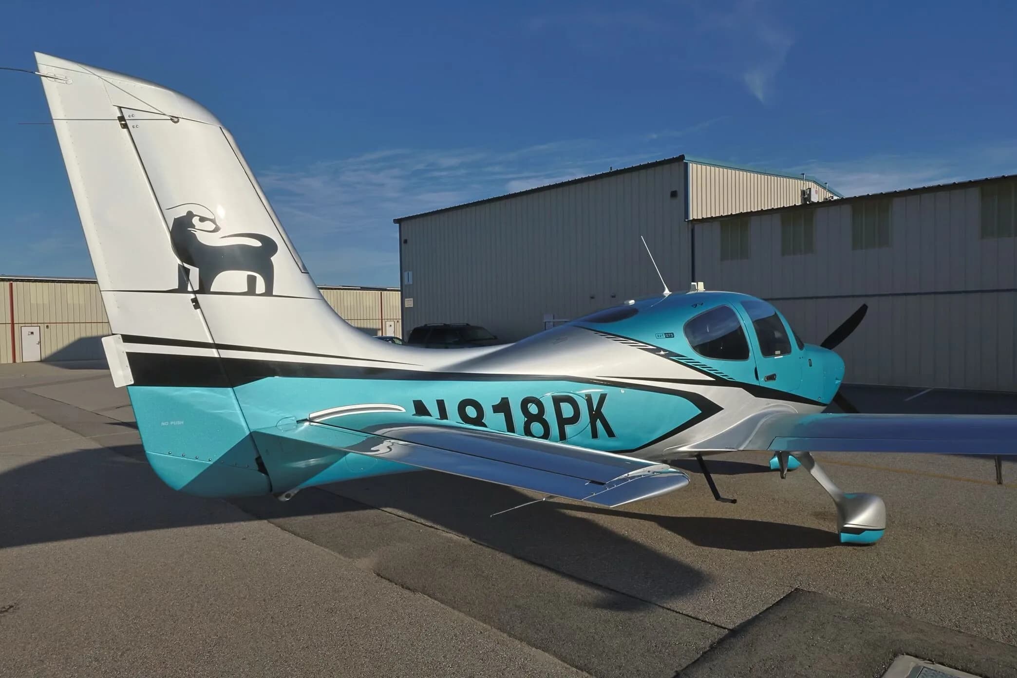 A rear three-quarter view of a teal and silver Cirrus SR22T GTS aircraft (N818PK) showing the tail and registration.
