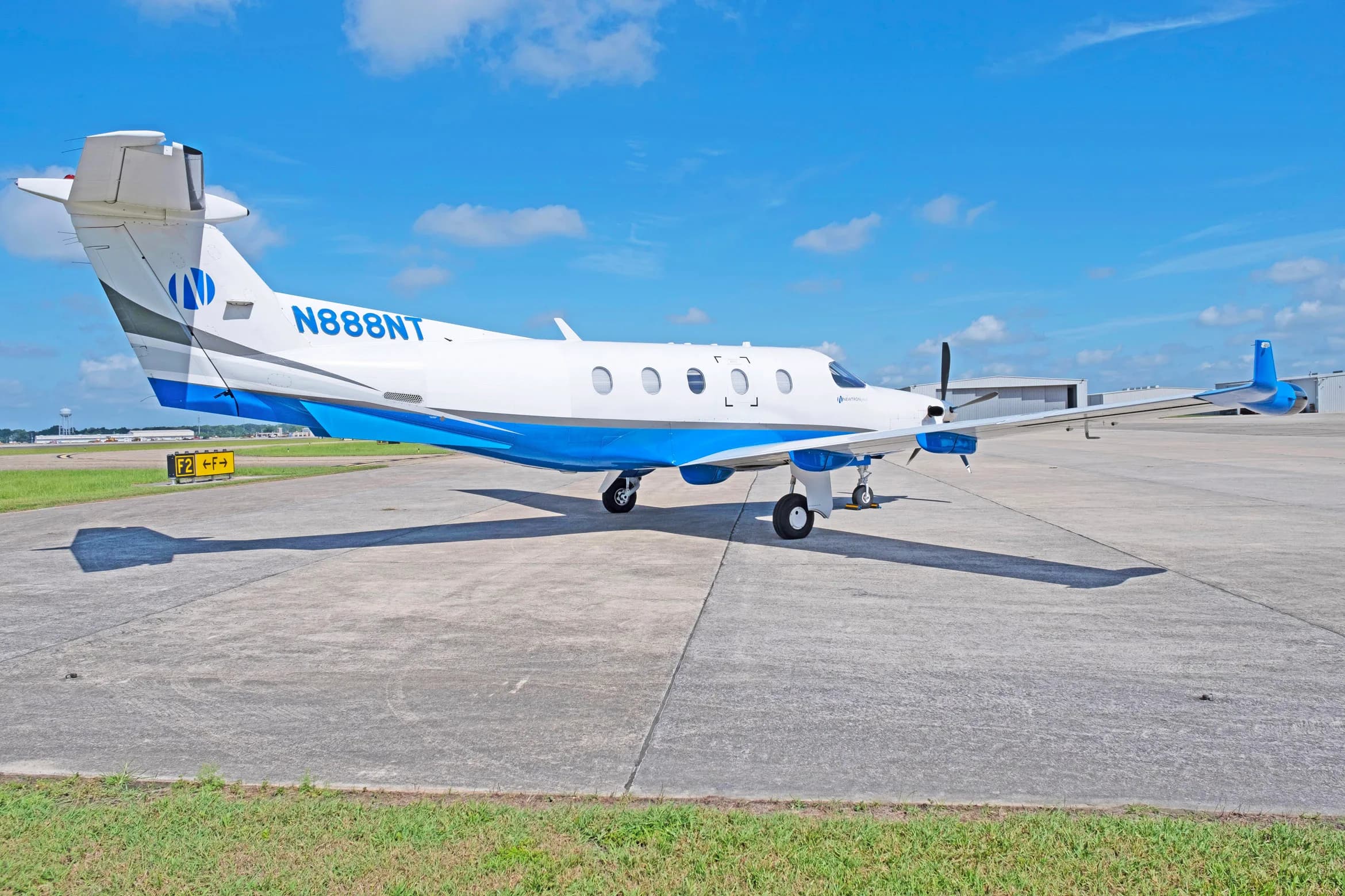 A white and blue Pilatus PC-12 aircraft, tail number N888NT, parked on a tarmac from a rear-side angle.