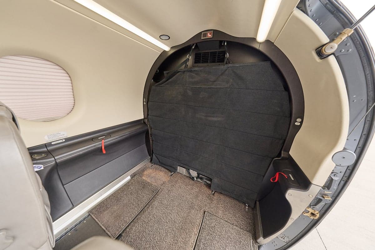 The interior of an aircraft cabin showing a rear cargo area with a black privacy curtain and light-colored walls.